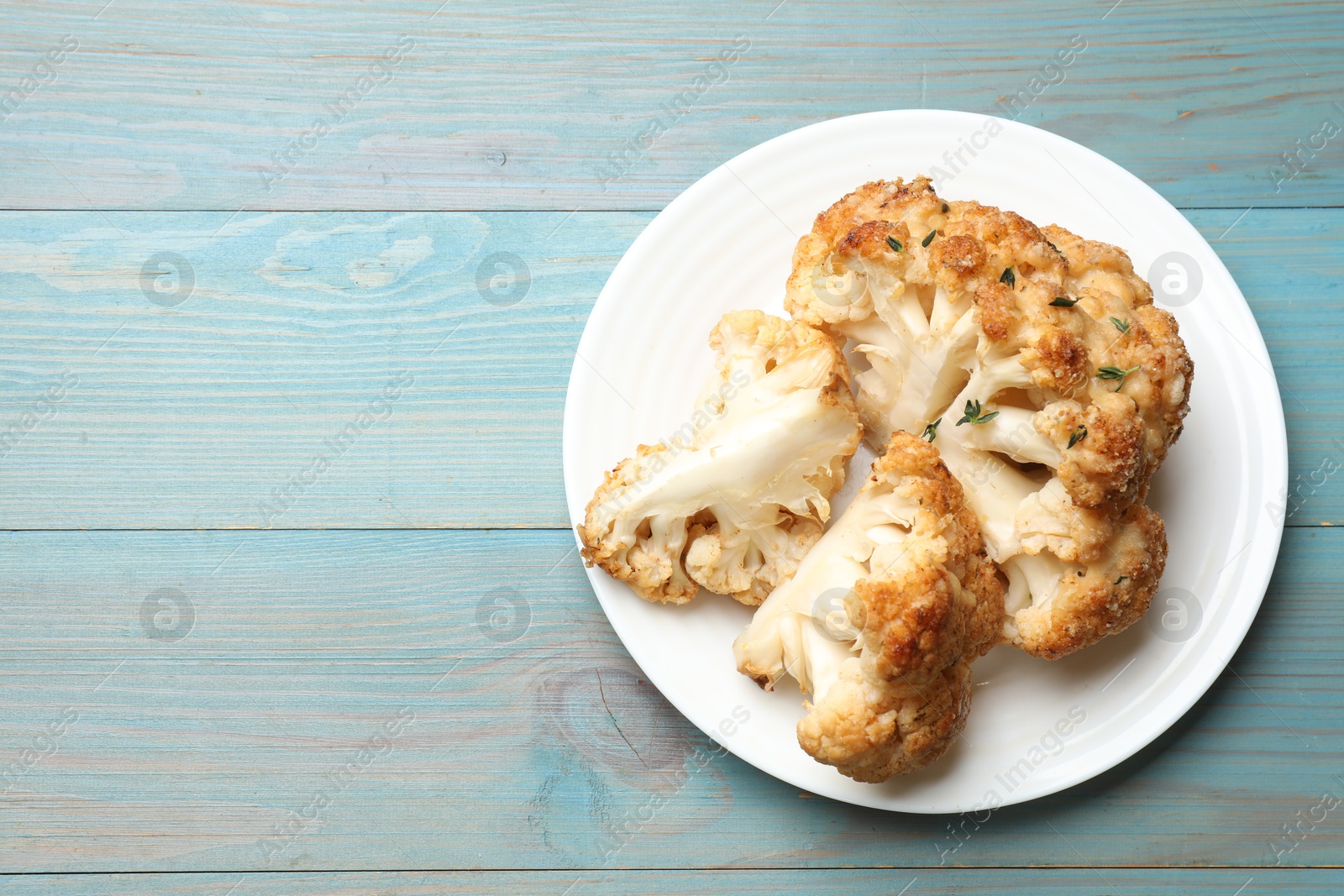 Photo of Plate with tasty baked cauliflower on light blue wooden table, top view. Space for text