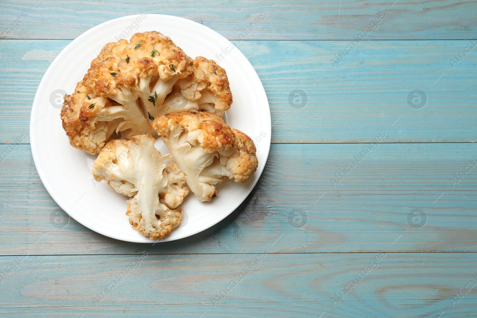 Photo of Plate with tasty baked cauliflower on light blue wooden table, top view. Space for text