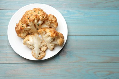 Plate with tasty baked cauliflower on light blue wooden table, top view. Space for text