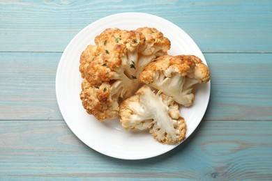 Plate with tasty baked cauliflower on light blue wooden table, top view