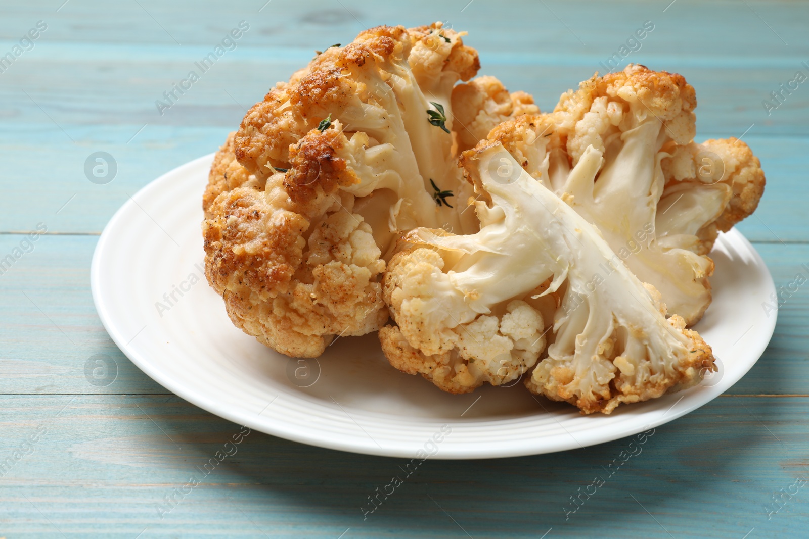 Photo of Plate with tasty baked cauliflower on light blue wooden table, closeup