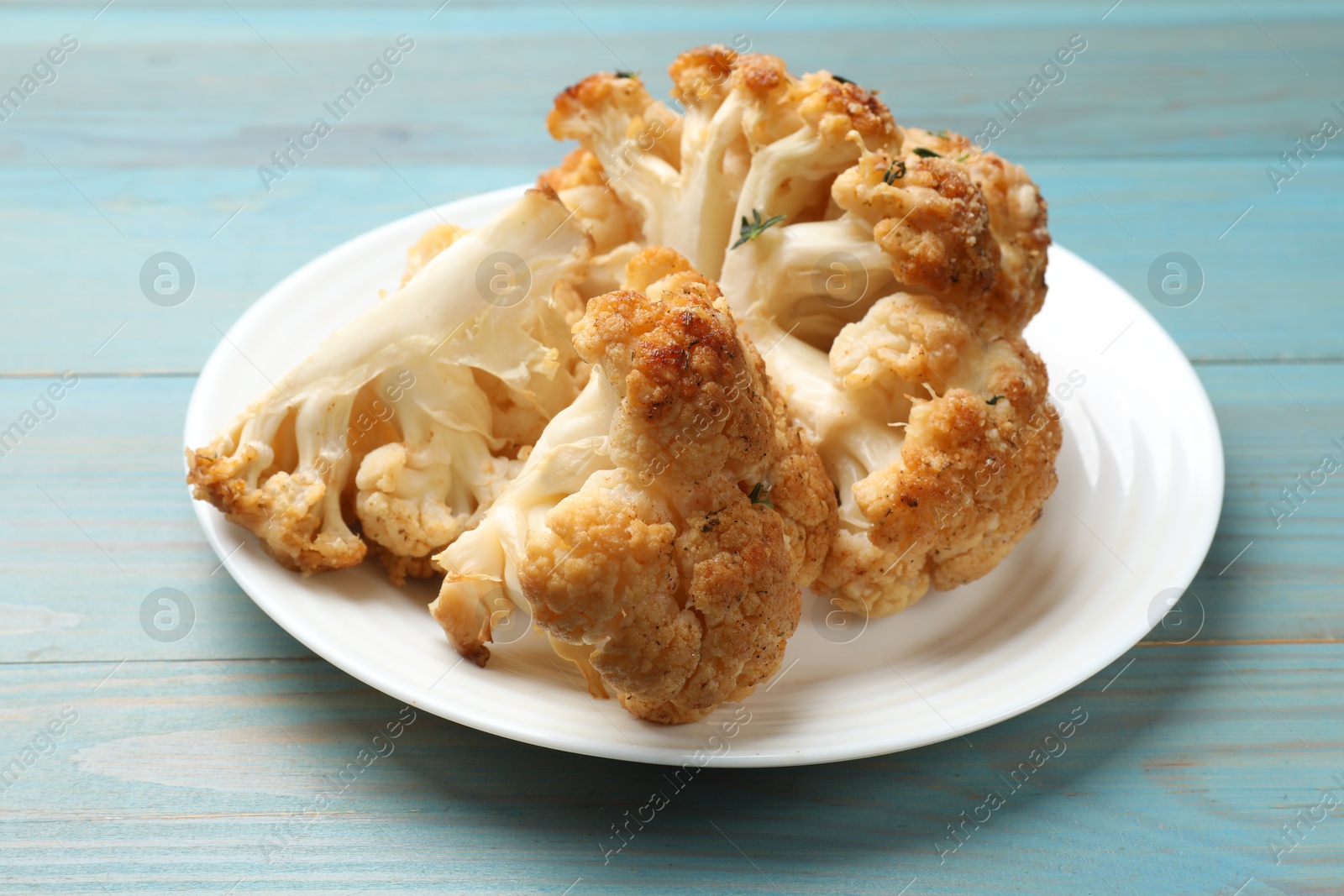 Photo of Plate with tasty baked cauliflower on light blue wooden table, closeup