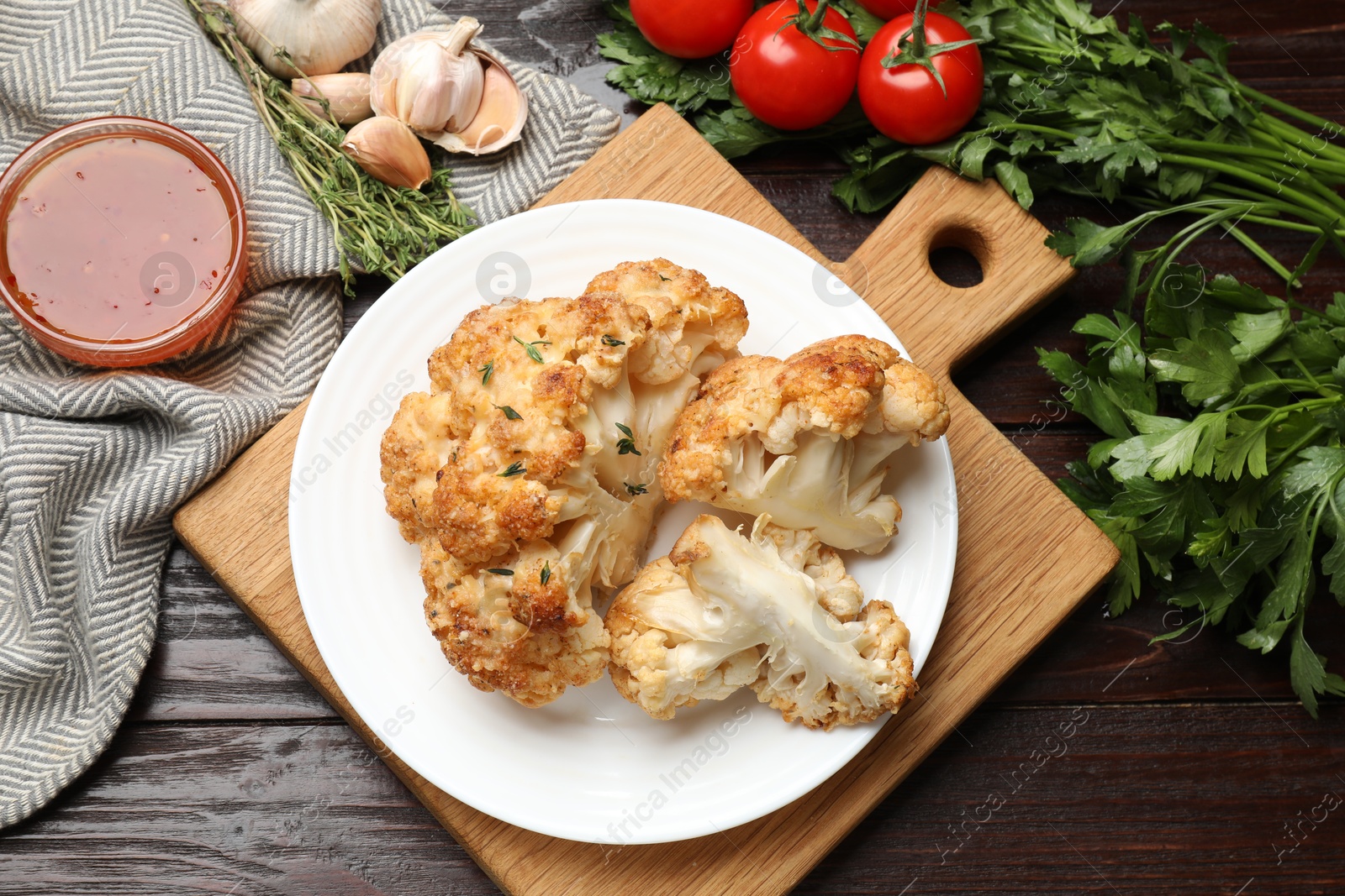 Photo of Plate with tasty baked cauliflower, sauce and products on wooden table, flat lay