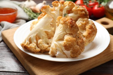 Photo of Plate with tasty baked cauliflower on wooden table, closeup