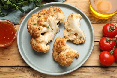 Photo of Plate with tasty baked cauliflower, sauce and products on wooden table, flat lay