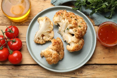 Plate with tasty baked cauliflower, sauce and products on wooden table, flat lay