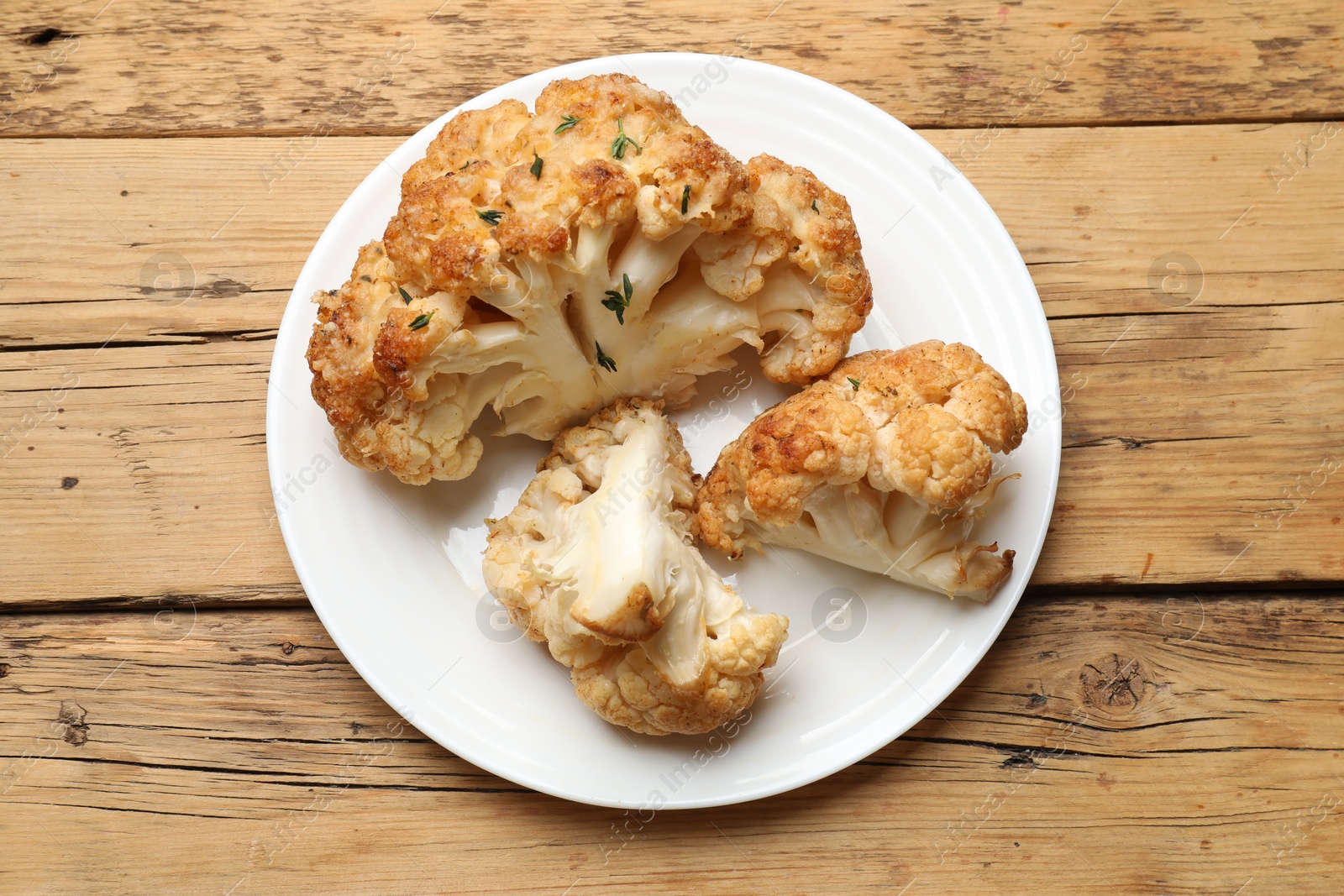 Photo of Plate with tasty baked cauliflower on wooden table, top view