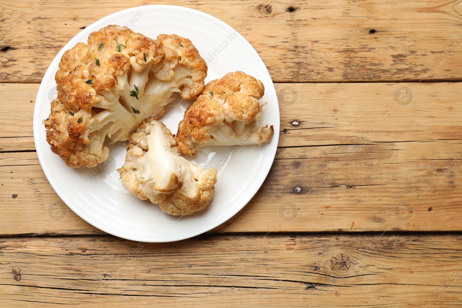 Photo of Plate with tasty baked cauliflower on wooden table, top view. Space for text