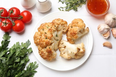 Photo of Plate with tasty baked cauliflower, sauce and products on white tiled table, flat lay