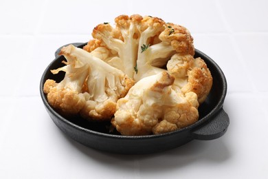 Photo of Tasty baked cauliflower in baking pan on white tiled table, closeup