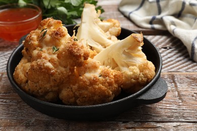 Tasty baked cauliflower in baking pan on wooden table, closeup