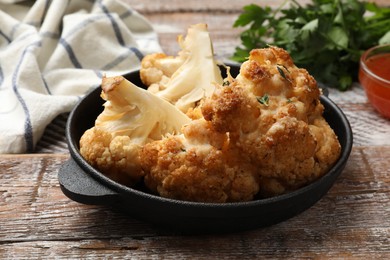 Photo of Tasty baked cauliflower in baking pan on wooden table, closeup