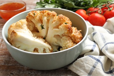 Photo of Tasty baked cauliflower in bowl on wooden table, closeup