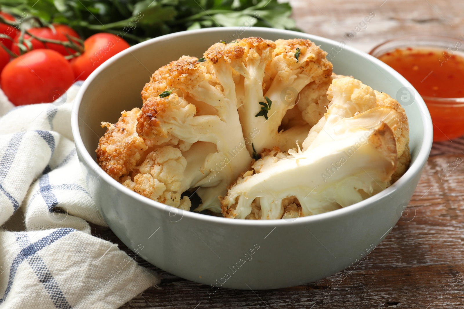 Photo of Tasty baked cauliflower in bowl on wooden table, closeup