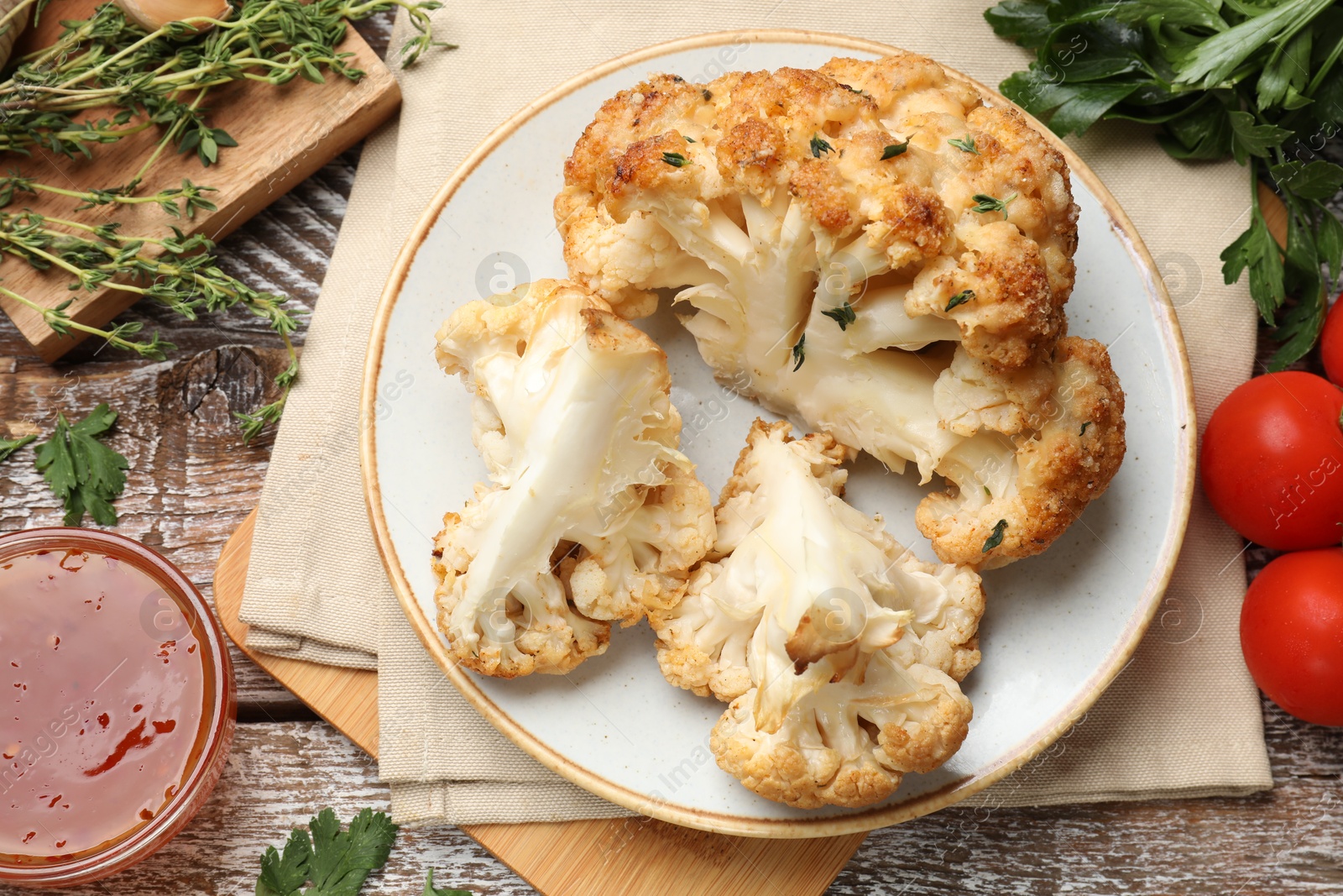 Photo of Plate with tasty baked cauliflower, sauce and products on wooden table, flat lay