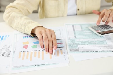 Budget planning. Woman with papers using calculator at white table, closeup