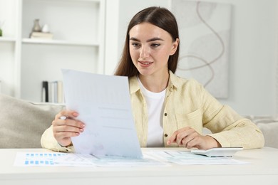 Budget planning. Beautiful young woman with papers and calculator at white table indoors