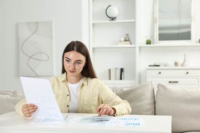 Photo of Budget planning. Beautiful young woman with papers using calculator at white table indoors