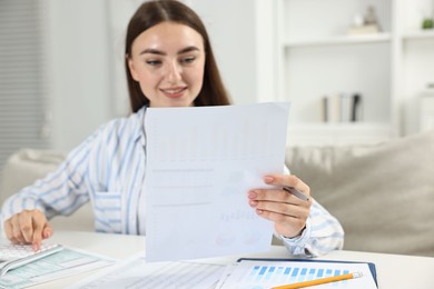 Budget planning. Beautiful young woman with papers using calculator at white table indoors, selective focus