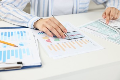 Budget planning. Woman with papers using calculator at white table, closeup