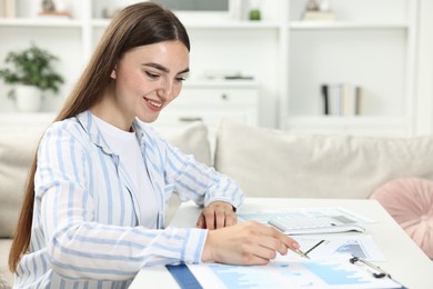 Photo of Budget planning. Beautiful young woman with papers and calculator at white table indoors