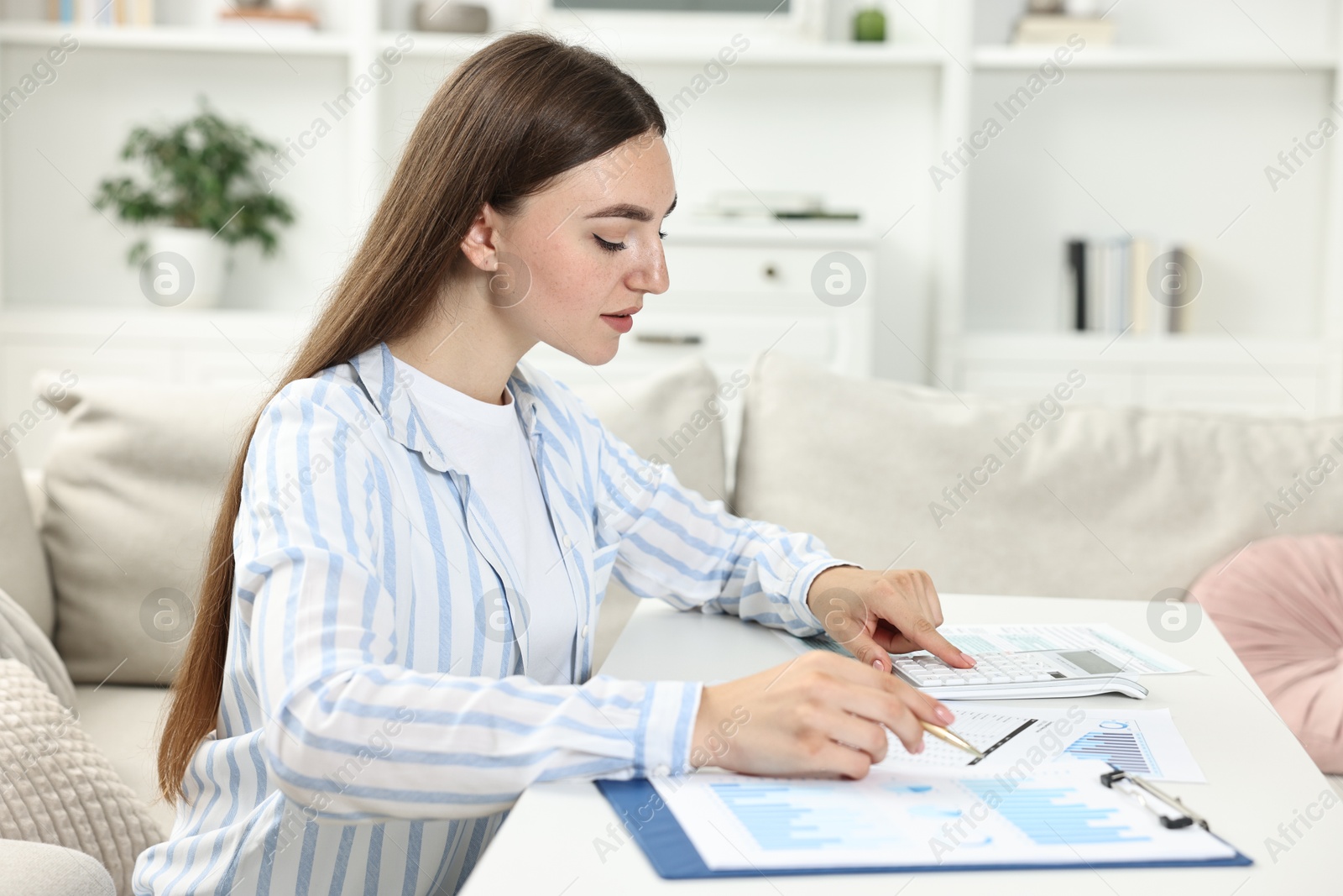 Photo of Budget planning. Beautiful young woman with papers using calculator at white table indoors