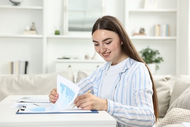 Photo of Budget planning. Beautiful young woman with papers at white table indoors