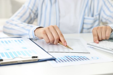 Budget planning. Woman with papers using calculator at white table, closeup