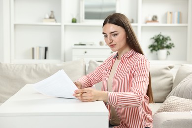 Budget planning. Beautiful young woman with papers at white table indoors