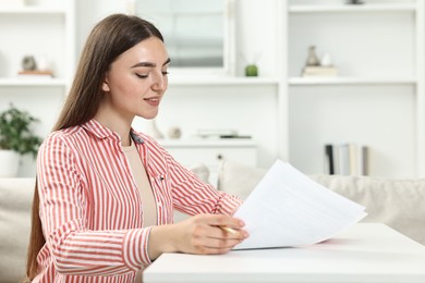 Photo of Budget planning. Beautiful young woman with papers at white table indoors