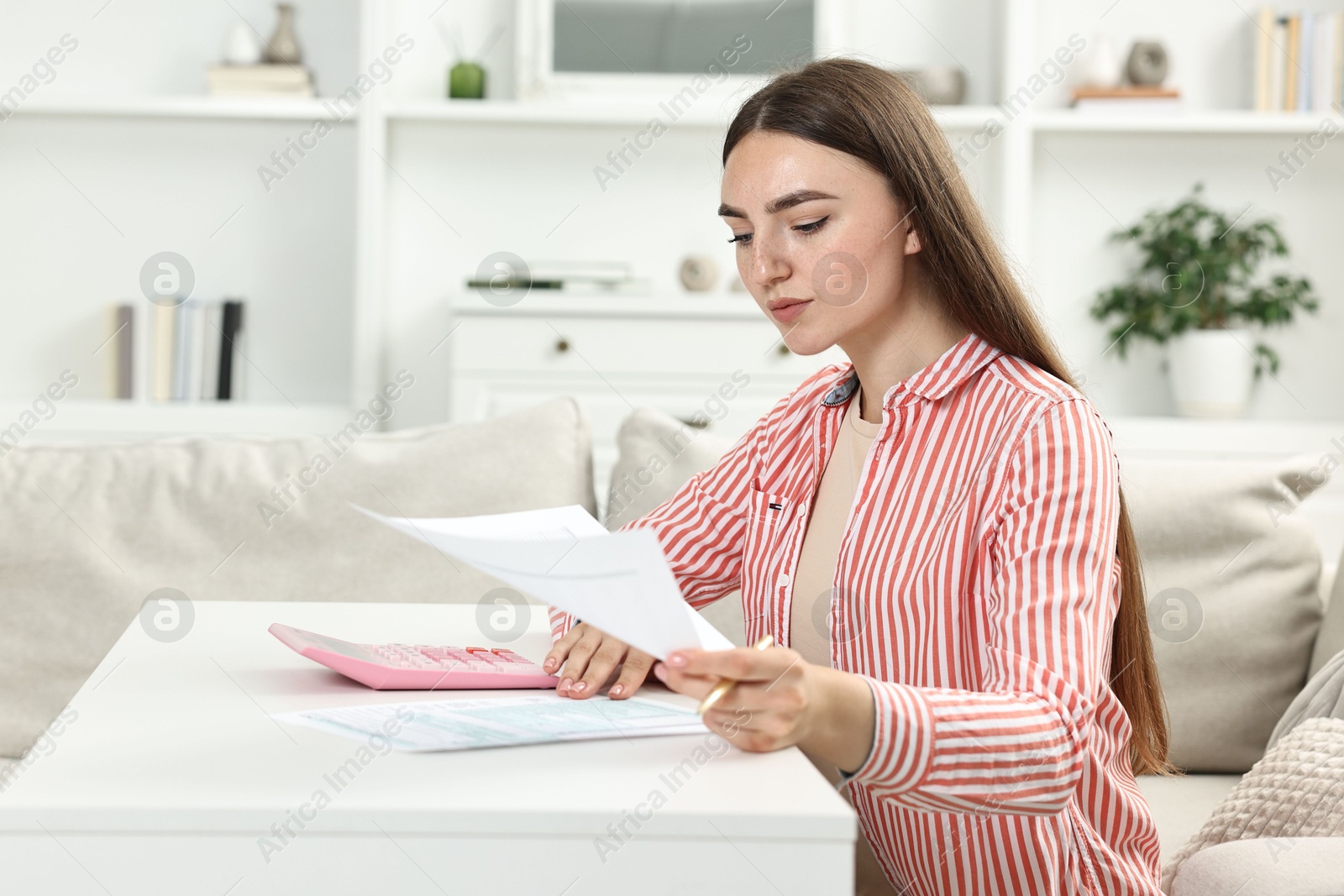 Photo of Budget planning. Beautiful young woman with papers and calculator at white table indoors