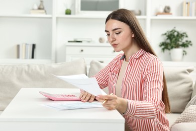 Budget planning. Beautiful young woman with papers and calculator at white table indoors