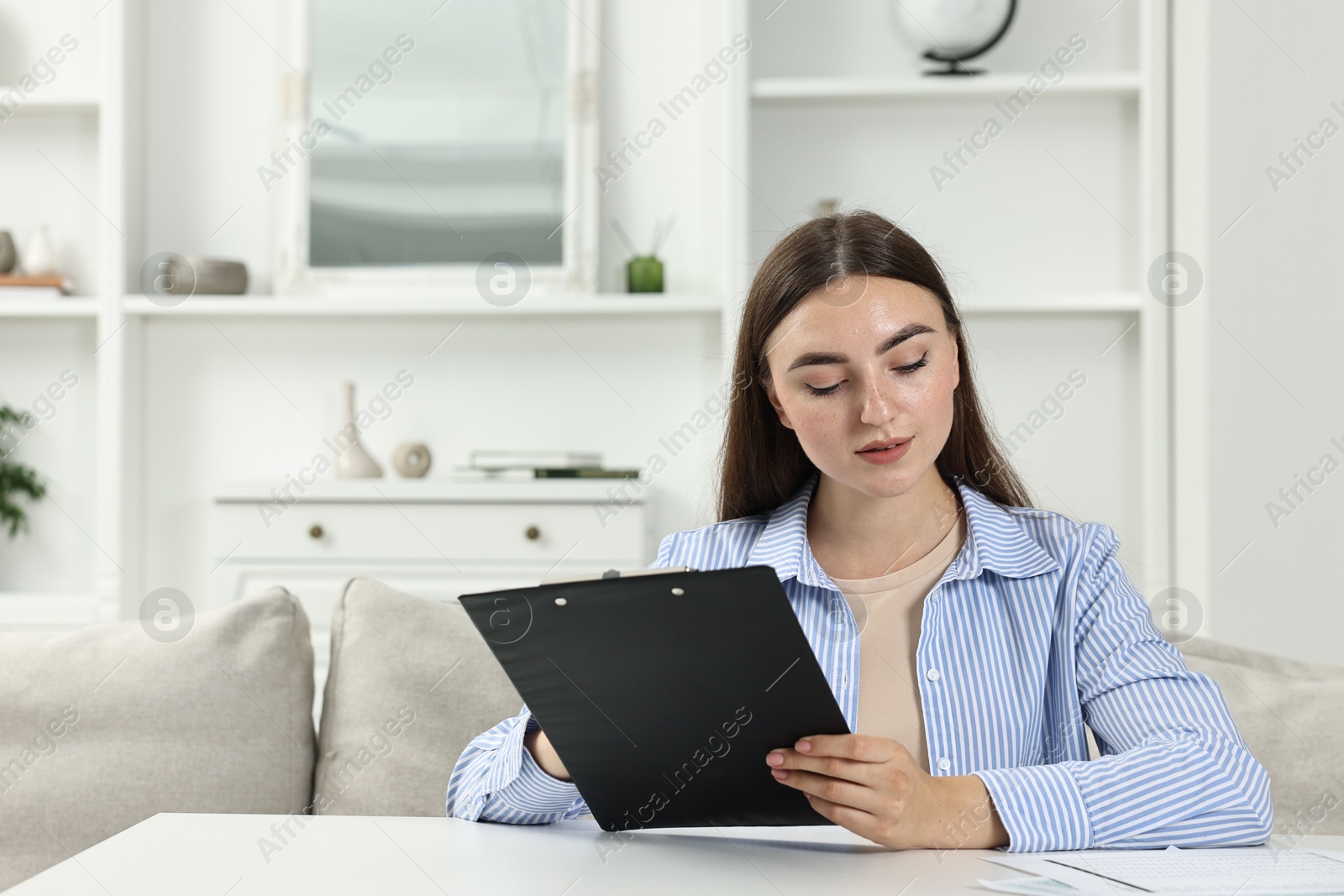 Photo of Budget planning. Beautiful young woman with papers at white table indoors