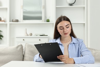 Photo of Budget planning. Beautiful young woman with papers at white table indoors