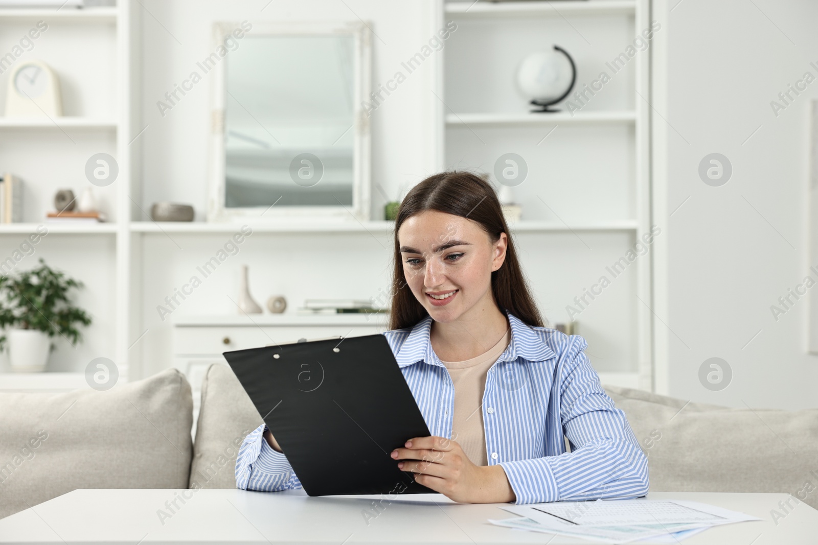 Photo of Budget planning. Beautiful young woman with papers at white table indoors