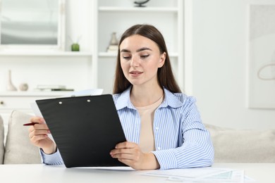 Photo of Budget planning. Beautiful young woman with papers at white table indoors