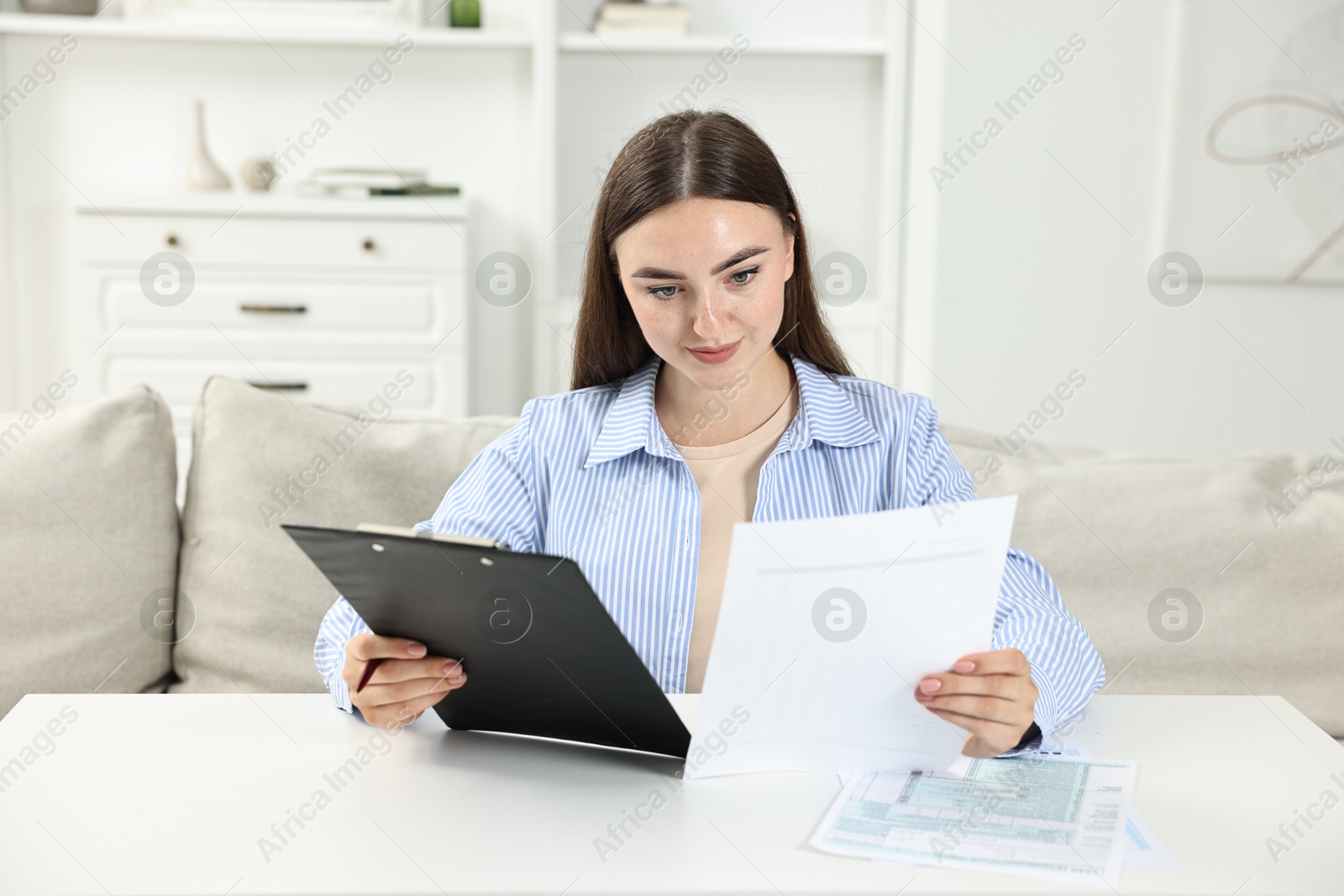 Photo of Budget planning. Beautiful young woman with papers at white table indoors