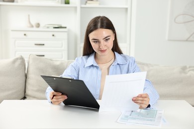 Photo of Budget planning. Beautiful young woman with papers at white table indoors