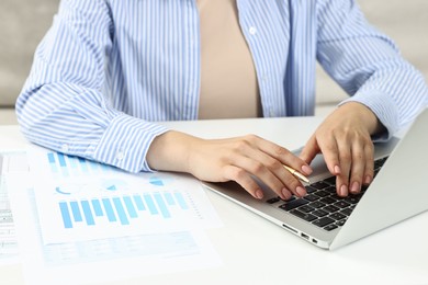 Budget planning. Woman with papers using laptop at white table, closeup