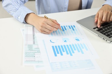 Budget planning. Woman with papers using laptop at white table, closeup