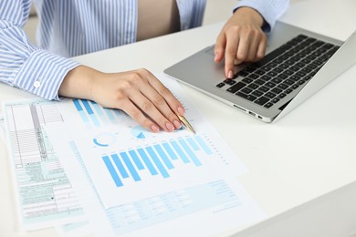 Budget planning. Woman with papers using laptop at white table, closeup