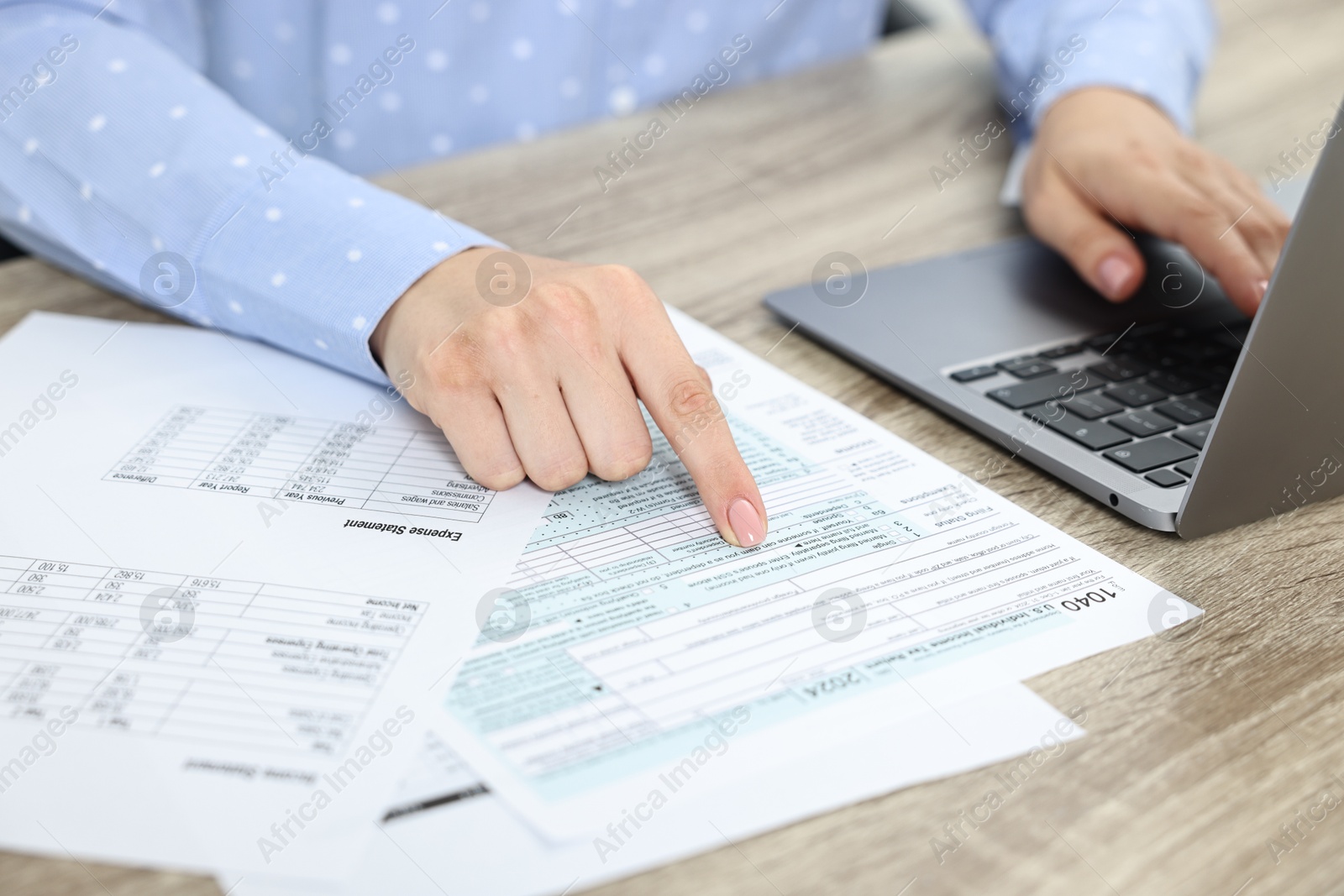 Photo of Budget planning. Woman with papers using laptop at wooden table, closeup