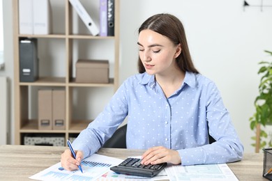 Photo of Budget planning. Beautiful young woman with papers using calculator at wooden table in office