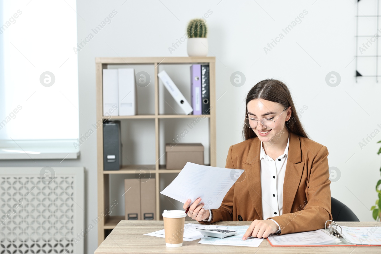 Photo of Budget planning. Beautiful young woman with papers and calculator at wooden table in office