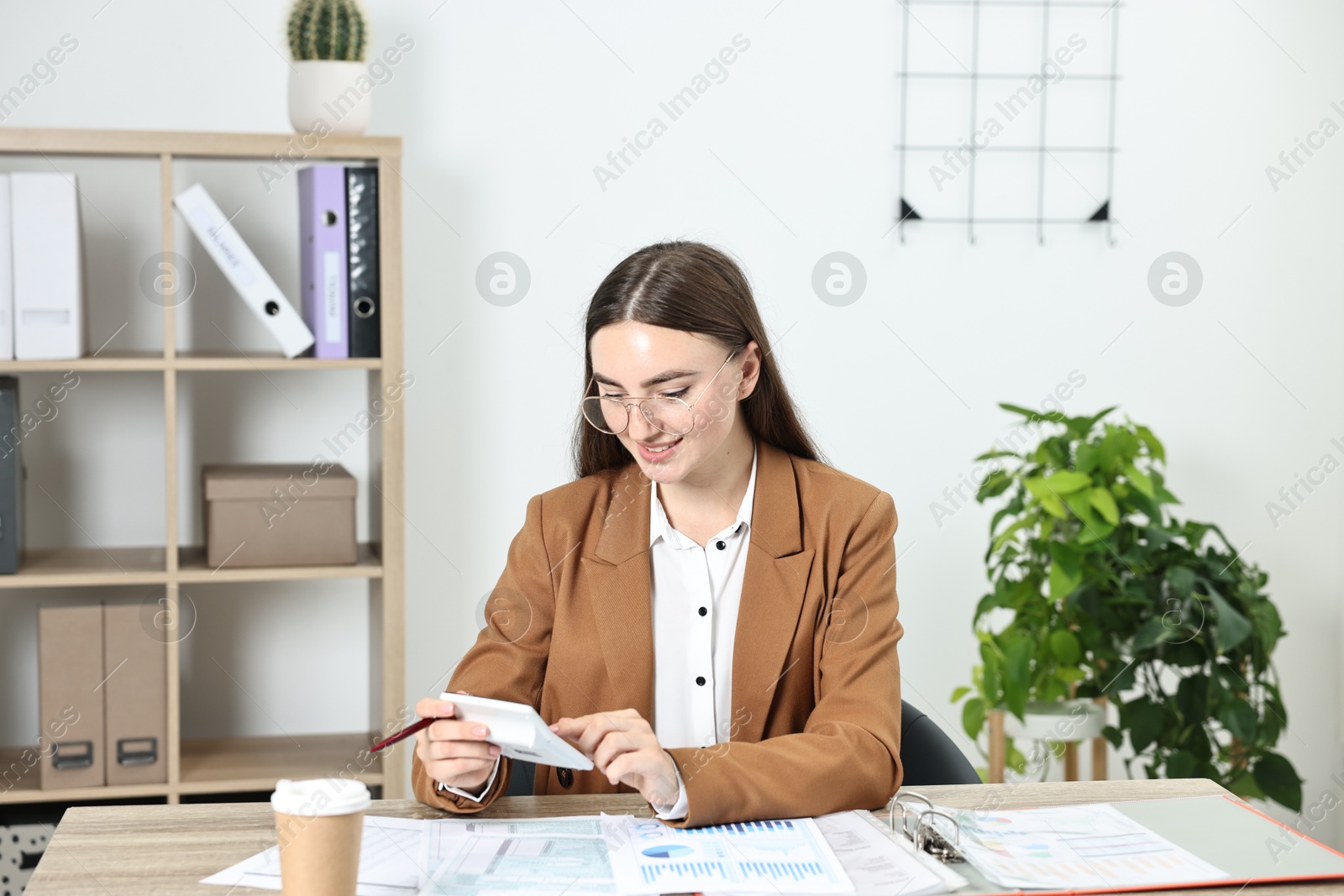 Photo of Budget planning. Young woman with papers using calculator at wooden table in office