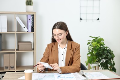 Budget planning. Young woman with papers using calculator at wooden table in office