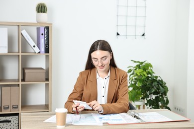 Budget planning. Beautiful young woman with papers using calculator at wooden table in office