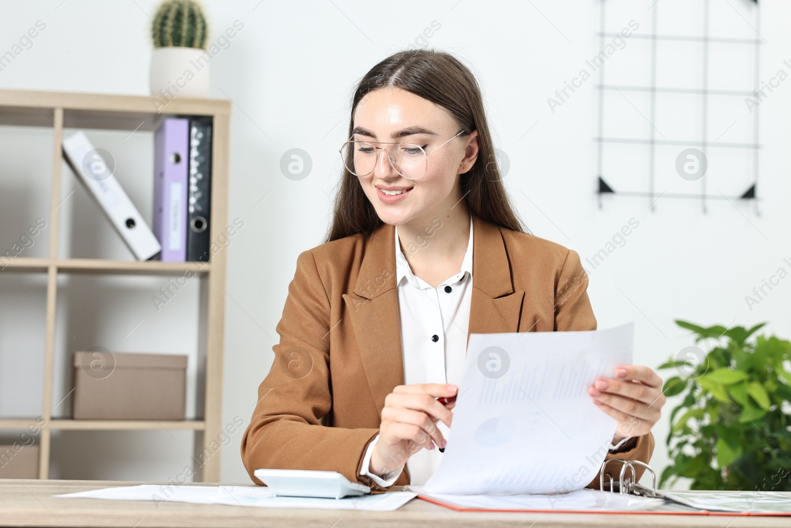 Photo of Budget planning. Beautiful young woman with papers and calculator at wooden table in office