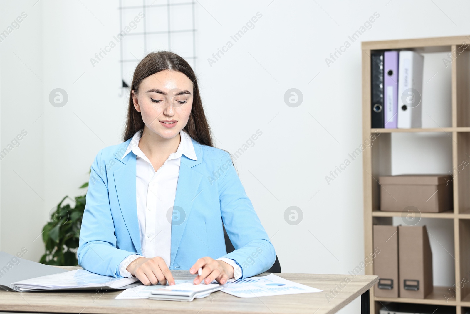 Photo of Budget planning. Beautiful young woman with papers and calculator at wooden table in office