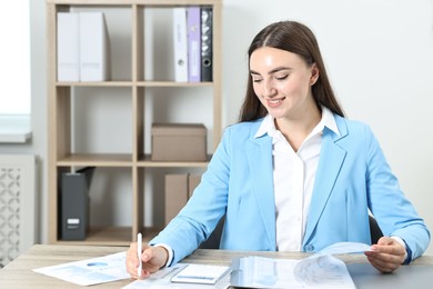 Photo of Budget planning. Beautiful young woman with papers and calculator at wooden table in office